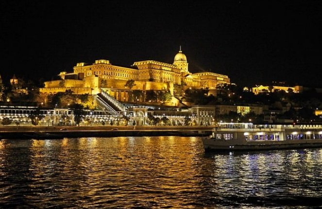Castelo de Buda iluminado e barco passando no rio Danúbio