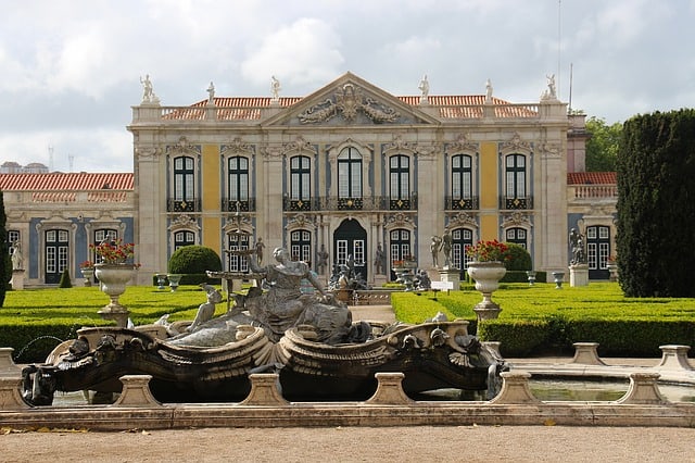 Palácio Queluz Palácio com dois andares, monumentos no topo e jardim na frente