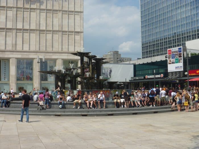 O movimento na Alexanderplatz Fonte com pessoas sentadas na Alexanderplatz, em Berlim