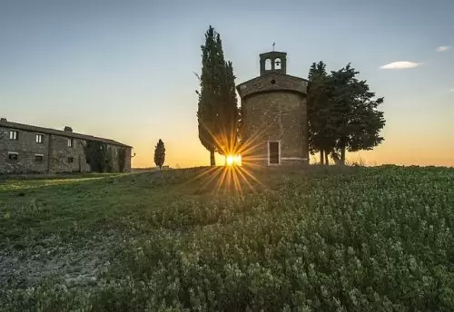 Campo gramado com igreja pequena e sol se pondo ao fundo